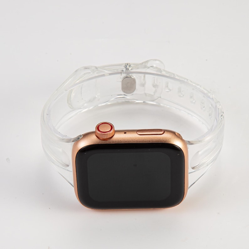 K&ouml;nnte beinhalten: Eine Apple Watch in Ros&eacute;gold mit einem klaren, strukturierten Silikonarmband. Das Zifferblatt der Uhr ist schwarz und das Armband hat einen Schlie&szlig;enverschluss.