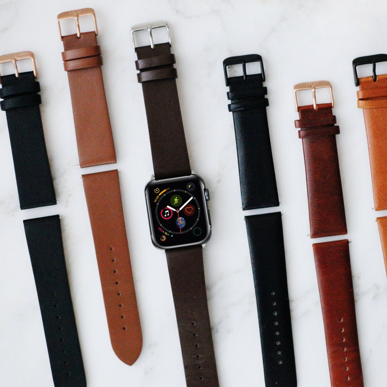 May include: A collection of leather watch straps in black, tan, and dark brown, featuring metal buckles in silver, gold, and black finishes. One dark brown strap is attached to a digital smartwatch with a circular app icon display.