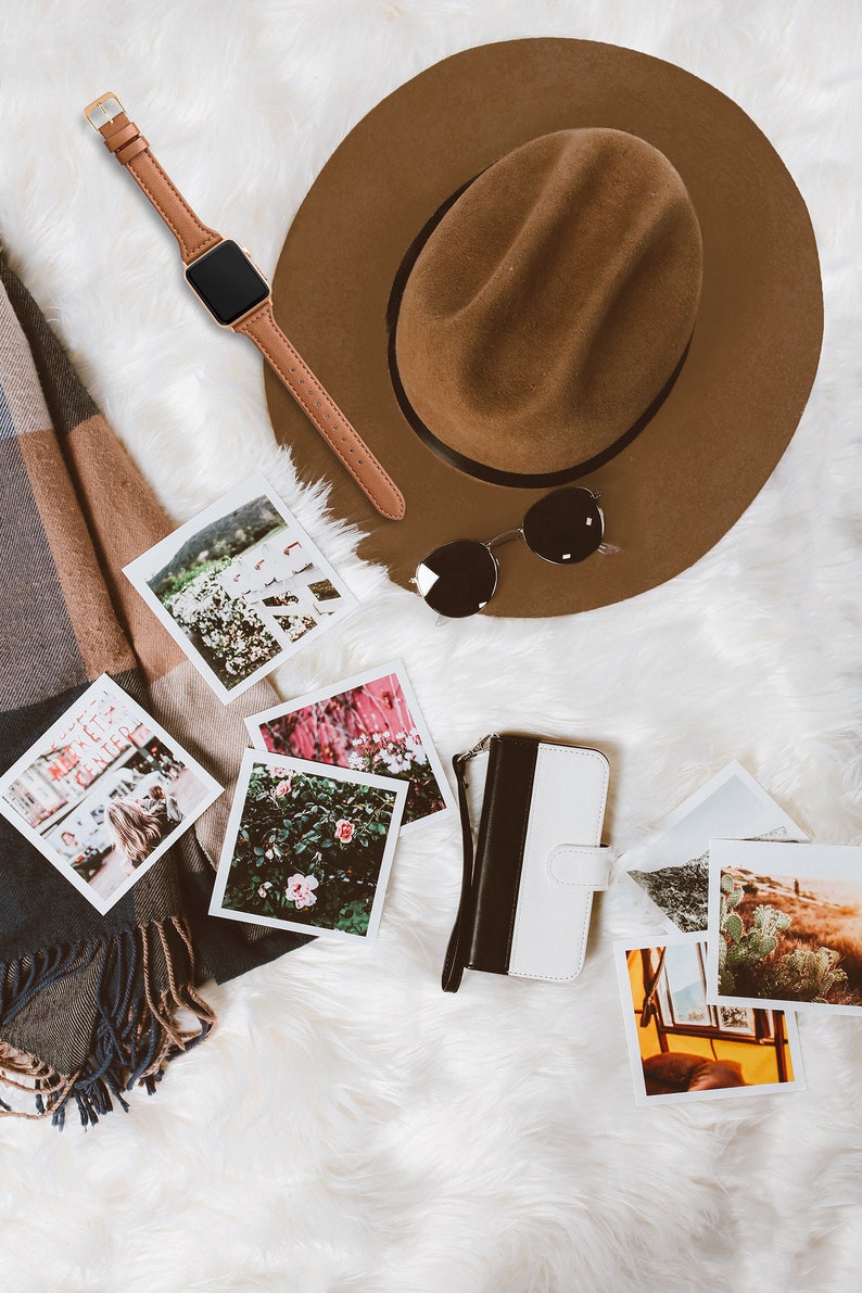 May include: A brown fedora hat, sunglasses, a brown leather watch, a black and white phone case, a scarf, and several square photographs are arranged on a white, fluffy surface. The photographs depict various scenes.