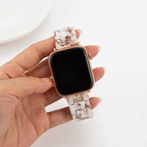 May include: A white and rose gold Apple Watch with a white marble-patterned band.