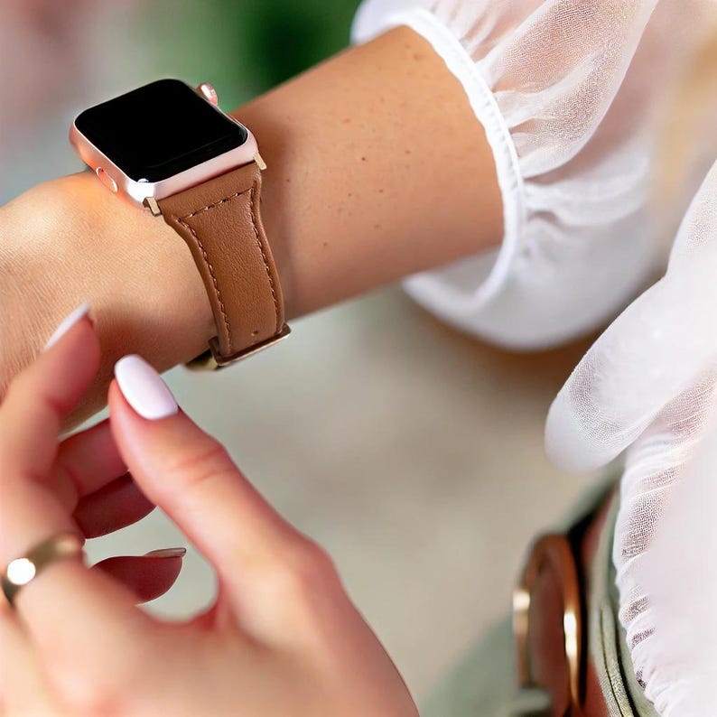 May include: A rose gold Apple Watch with a brown leather band. The watch is on a person's wrist.