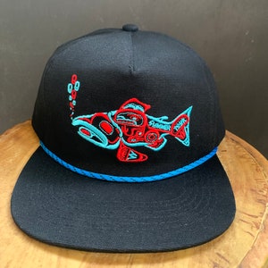May include: Black baseball cap with a blue rope trim and a red and blue embroidered salmon design. The salmon is stylized with geometric shapes and the text "SUMMER" and "TRUNK" is embroidered on the fish.