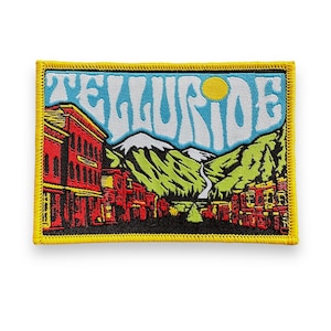 May include: Rectangular patch with a yellow border featuring a colorful illustration of Telluride. The design includes red buildings, green mountains, a blue sky with the word "TELLURIDE" in white, and a yellow sun.