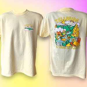 May include: A yellow t-shirt with a cartoon illustration of a fox playing a banjo in a mountain scene. The back of the shirt says "Telluride, A Town of Plenty".