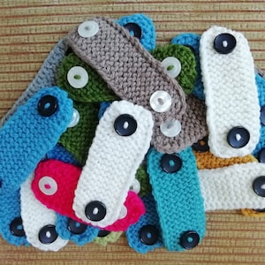 May include: A pile of colourful knitted mask extenders with buttons. The extenders are made in various colours, including blue, green, white, brown, and yellow.