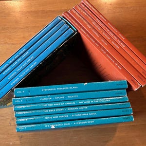May include: A collection of vintage children's books in blue and orange. The titles include "Stories, Tales and Fables" and classic literature like "Treasure Island" and "A Christmas Carol". The books are arranged in stacks and boxes.