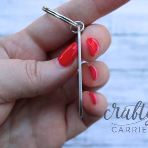 May include: Silver key ring with a rectangular tag. The tag is blank and has a brushed metal finish. The keyring is held in a hand with red nail polish.