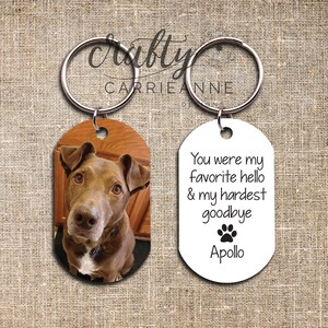 May include: A white oval keyring with the text "You were my favourite hello & my hardest goodbye" and a paw print. The text "Apollo" is below the paw print. A second oval keyring features a photo of a brown dog.