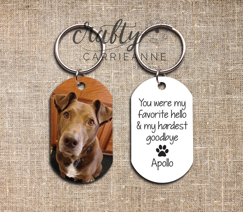May include: A white oval keyring with the text "You were my favourite hello & my hardest goodbye" and a paw print. The text "Apollo" is below the paw print. A second oval keyring features a photo of a brown dog.