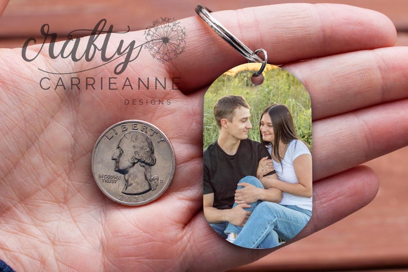May include: A silver keychain with a photo of a couple in a field. The photo is oval shaped and the keychain is in the palm of a hand.