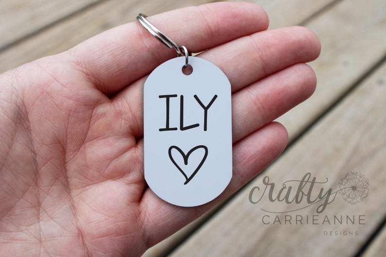 May include: A white metal keychain with a silver key ring. The keychain has the text "ILY" with a heart drawn below it.