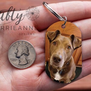 May include: A brown and white dog with a black collar is featured on a brown oval-shaped keyring. The keyring is attached to a silver key ring. A quarter is shown for size comparison.