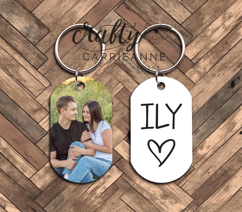May include: A set of two keychains. One keychain features a photo of a couple in a field. The other keychain is white with black text that says "ILY" with a heart.