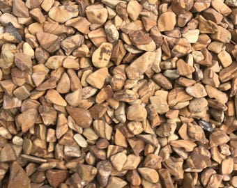 May include: A close-up view of a pile of small, brown and tan tumbled stones. The stones are smooth and have a natural, earthy look.
