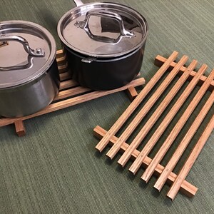 Puede incluir: Dos ollas de plata con tapas sobre un soporte para ollas de madera. El soporte para ollas es de madera marr&oacute;n claro y tiene forma rectangular.