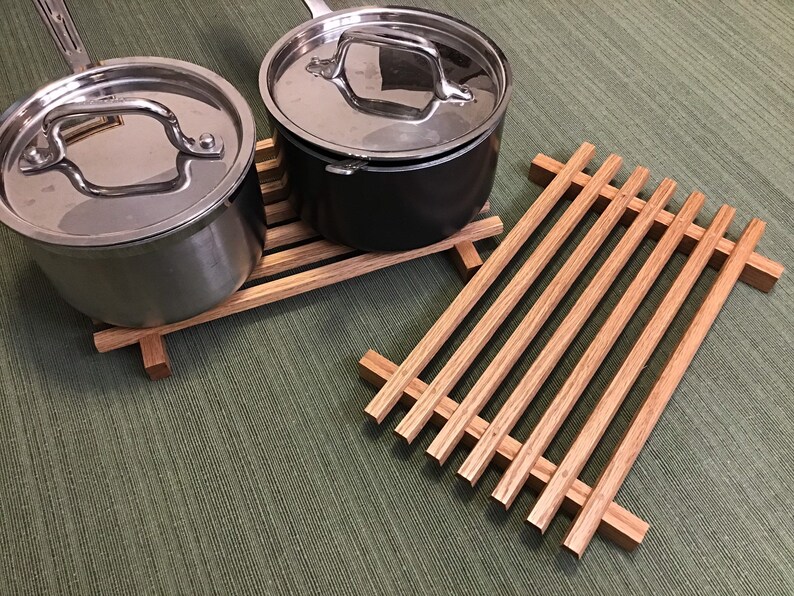 Puede incluir: Dos ollas de plata con tapas sobre un soporte para ollas de madera. El soporte para ollas es de madera marr&oacute;n claro y tiene forma rectangular.