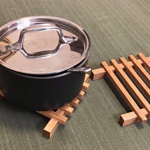 Puede incluir: Una olla de acero inoxidable con tapa se encuentra sobre un posavasos de madera. Un segundo posavasos de madera est&aacute; a la derecha de la olla.