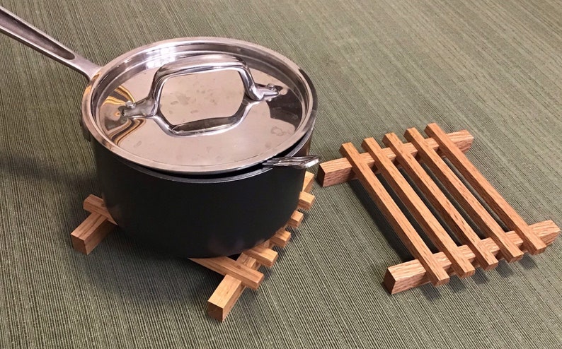 Puede incluir: Una olla de acero inoxidable con tapa se encuentra sobre un posavasos de madera. Un segundo posavasos de madera est&aacute; a la derecha de la olla.