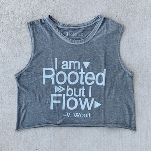 May include: Gray sleeveless crop top with the text "I am Rooted but I Flow - V. Woolf" in white. The top has a rounded neckline and a raw, unfinished hemline. The fabric appears to be soft and slightly faded.