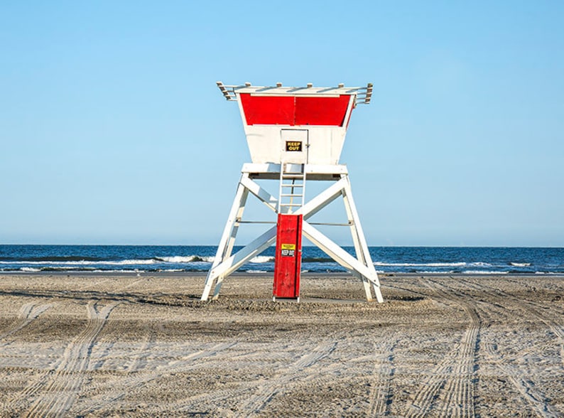 Puede incluir: Un puesto de socorrismo blanco y rojo en una playa de arena con la inscripci&oacute;n "Keep Out" en la puerta.