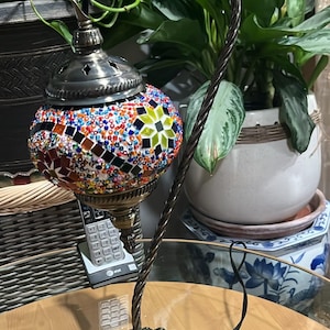 May include: A table lamp with a mosaic glass shade in shades of red, blue, green, and yellow. The lamp has a twisted metal base and a black cord.