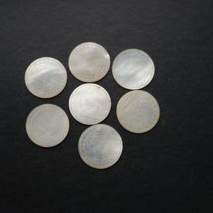 May include: Seven silver coins displayed on a dark surface. Each coin features a detailed design and a reflective surface. The coins are arranged in a circular pattern, showcasing their intricate details and circular shape against the dark backdrop.