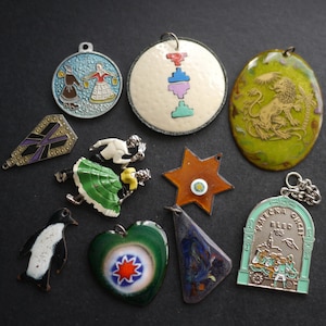 May include: A collection of ten assorted metal and enamel pendants and charms featuring various designs including a lion, a penguin, a heart, a star, a dancing couple, and a commemorative piece with the text Kmecka Ohcet Bled 85.