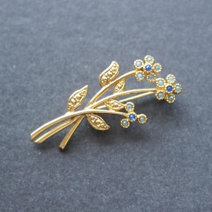 Gold tone flower brooch with blue rhinestones signed Movitex
