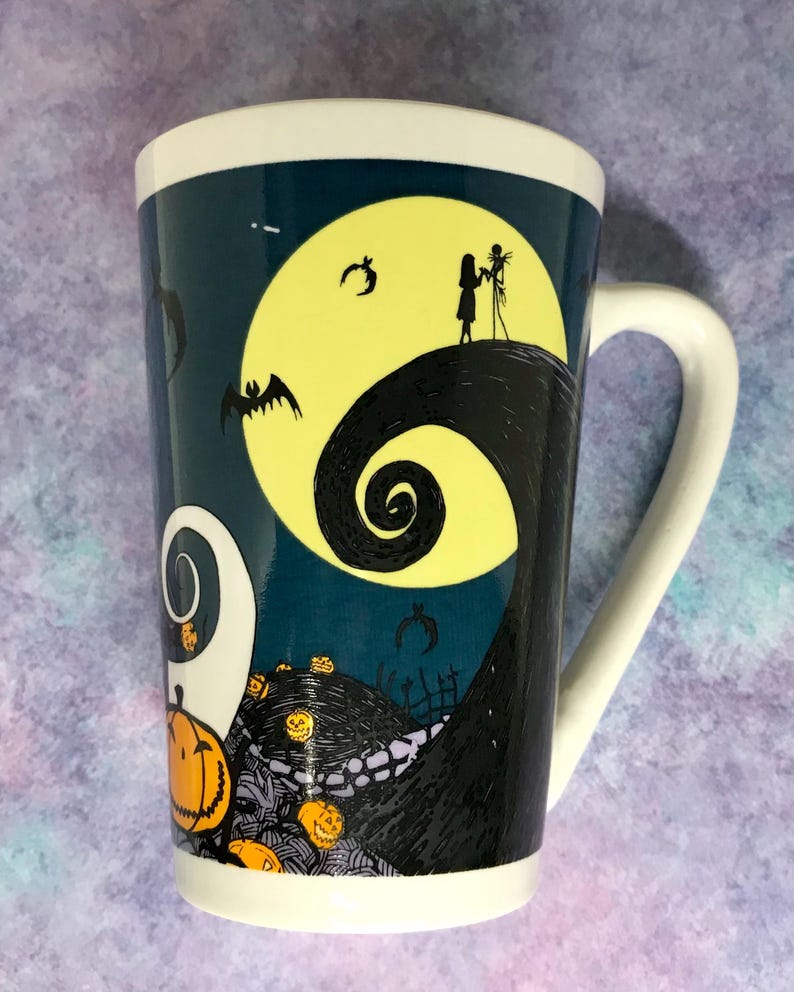 May include: Tall white ceramic mug featuring a design from The Nightmare Before Christmas. The mug has a dark teal background with a yellow full moon, Jack and Sally silhouettes, and swirling hill. Orange jack-o'-lanterns and bats are also featured.