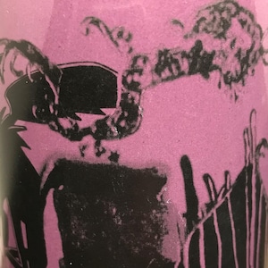 May include: A pink tumbler with a black graphic design. The design appears to be a stylized illustration of a person with a crown and a lightning bolt. The tumbler has a glossy finish.