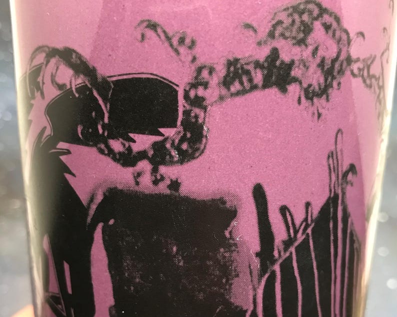 May include: A pink tumbler with a black graphic design. The design appears to be a stylized illustration of a person with a crown and a lightning bolt. The tumbler has a glossy finish.