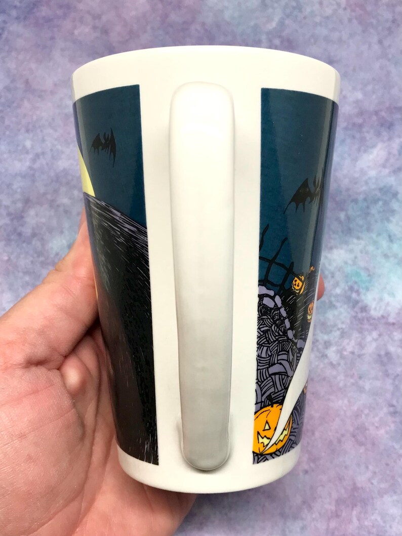 May include: White ceramic mug with a wraparound design featuring a spooky Halloween scene. The design includes a full moon, bats, and a graveyard with jack-o'-lanterns. The mug has a white handle.