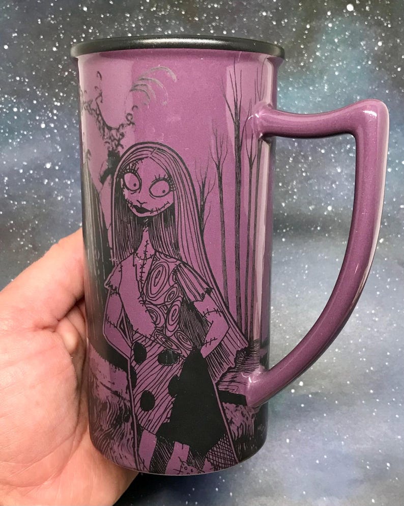 May include: Purple ceramic mug featuring a black and white illustration of Sally from The Nightmare Before Christmas. The mug has a matching purple handle and a black rim. The design includes trees and a spooky background.