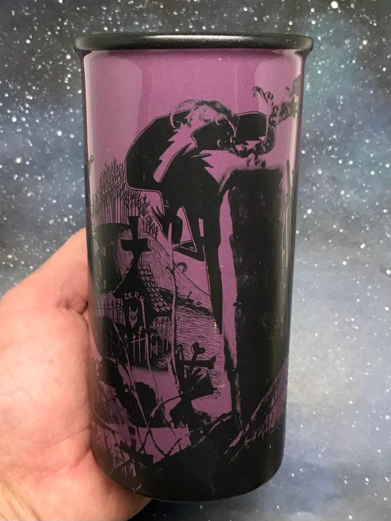 May include: A tall, black and purple tumbler featuring a spooky graveyard scene with a figure and the word "ZERO". The tumbler has a black rim and a purple interior, perfect for cold beverages.