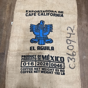 May include: A burlap coffee sack with the text "EXPORTADORA DE CAFE CALIFORNIA" and "EL AGUILA". A blue eagle graphic is centered on the bag. The text "PRODUCT OF MÉXICO" is printed below, along with the net weight of 152 lbs.