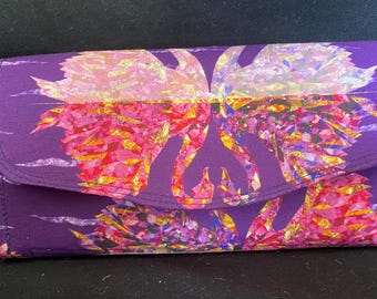 May include: A purple clutch purse with a colorful floral pattern. The pattern features pink, yellow, and blue flowers.