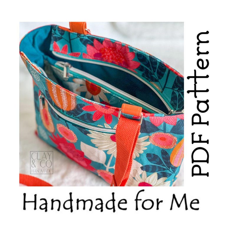 A floral tote bag with a teal background and orange accents. The bag features a colourful pattern of large flowers in pink, orange, and white. It has orange handles and the text "Handmade for Me" and "PDF Pattern".