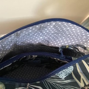 A top detail of a Phillippa Crossbody open made in fabric with a blue zip. The interior lining is grey with white polka dots. The exterior fabric features a dark blue floral pattern. The bag is open, showing the inside pocket. The bag was made using the Phillippa Crossbody sewing pattern.