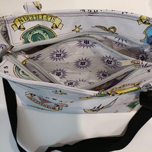 A detail of a light blue tote bag with a black strap, featuring a repeating pattern of Hogwarts crests and symbols. The bag has two zippered compartments and a light-coloured interior with a starburst pattern. The bag has a top handle and was made using the Phillippa Crossbody sewing pattern.