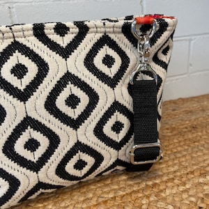 A black and white geometric pattern crossbody bag with a black strap and silver-tone hardware. The bag features a diamond pattern and a red accent on the interior. The bag is made of woven fabric and was made using the Phillippa Crossbody sewing pattern.