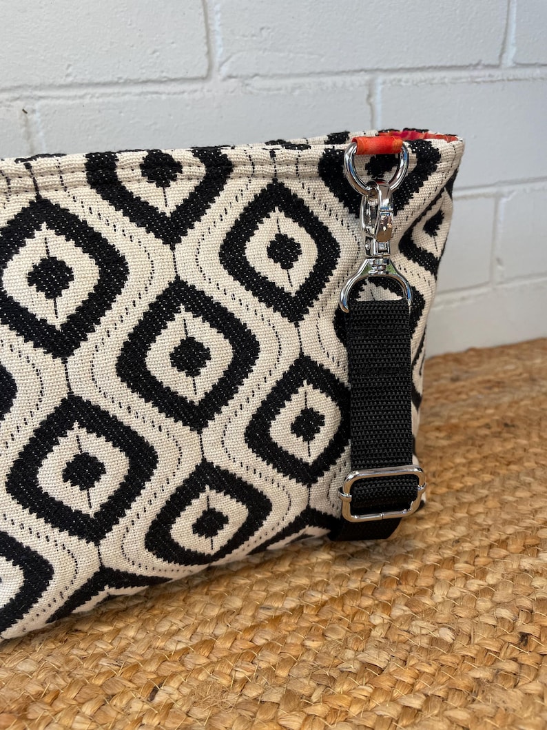 A black and white geometric pattern crossbody bag with a black strap and silver-tone hardware. The bag features a diamond pattern and a red accent on the interior. The bag is made of woven fabric and was made using the Phillippa Crossbody sewing pattern.