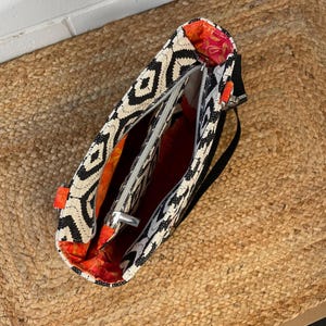 A detail of the top of a Phillippa Crossbody tote bag with a black and white geometric pattern and a black strap. The interior is lined with orange and red patterned fabric. The bag has a zip closure and an orange accent. The bag was made using the Phillippa Crossbody sewing pattern.