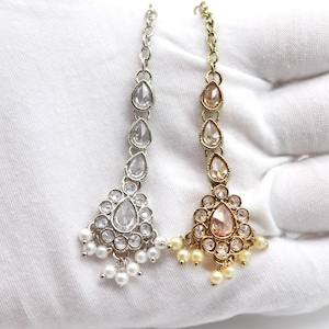 May include: Two silver and gold jeweled headpieces with pearl accents. The headpieces are on a white surface.