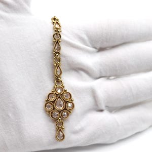 May include: A gold-toned chain with a teardrop-shaped pendant. The pendant is adorned with clear rhinestones in a circular design.