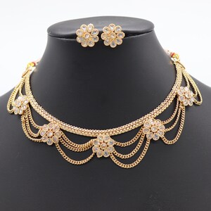May include: A gold necklace with a layered chain design and white flower accents. The necklace is paired with matching earrings.
