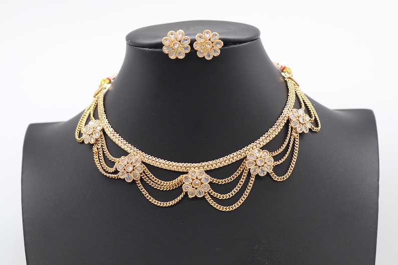 May include: A gold necklace with a layered chain design and white flower accents. The necklace is paired with matching earrings.
