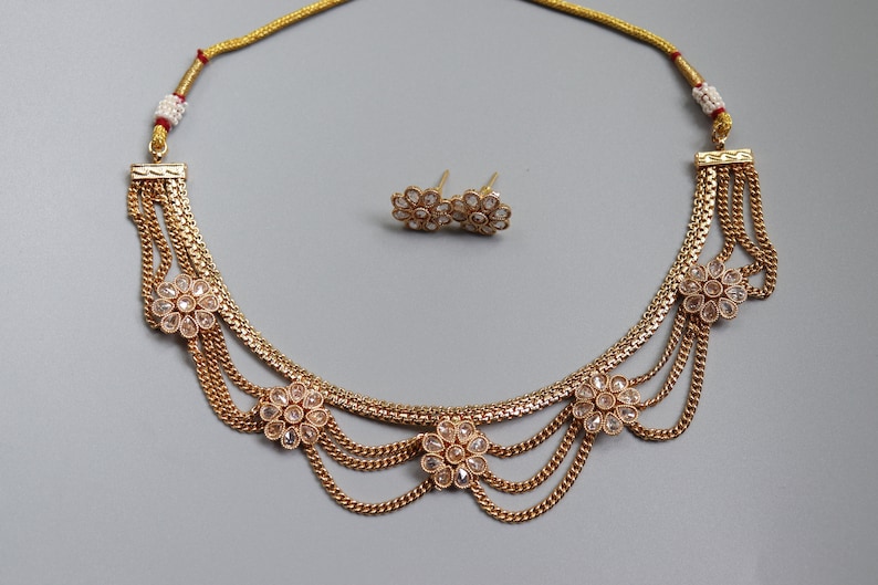May include: A gold necklace with multiple strands and clear crystal flower accents. Matching earrings with clear crystal flower accents are included.