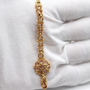 May include: A gold chain with a floral design at the bottom and small clear stones throughout.
