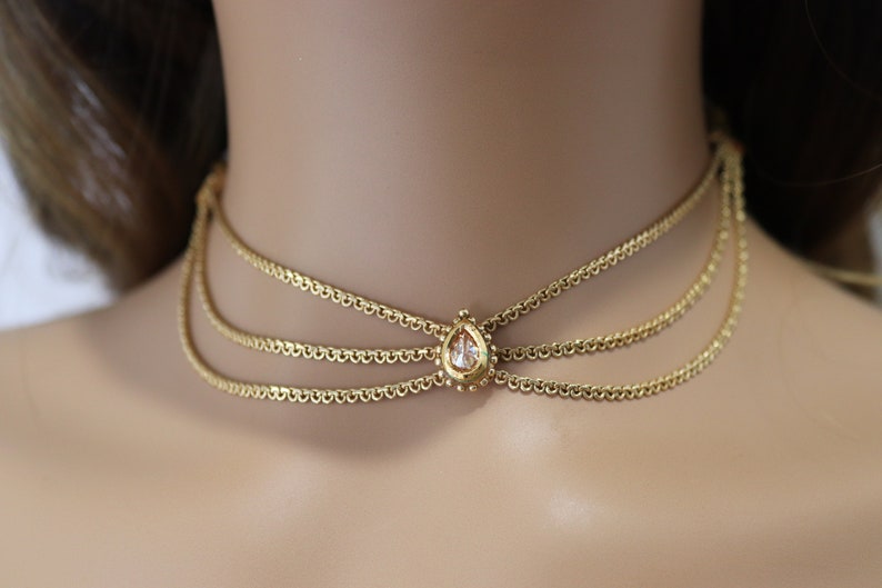 Pu&ograve; includere: Un girocollo dorato con tre catene delicate e un ciondolo di cristallo a forma di lacrima.
