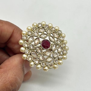 May include: A gold ring with a red stone in the center surrounded by white stones and pearls.